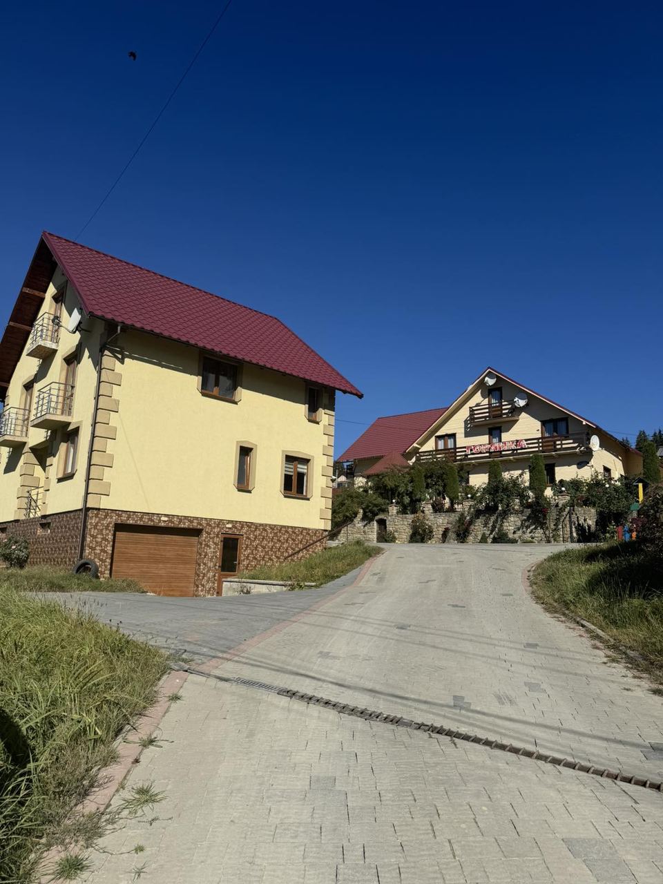 Два жовті будинки з червоними дахами вздовж бруківки